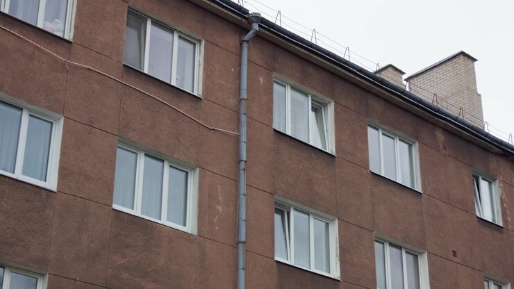 Tomada inclinada em ângulo baixo mostra a fachada pintada de marrom de um edifício de apartamentos residenciais de vários andares com calha e janelas de plástico brancas em Daugavpils, Letônia