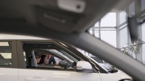 young car salesman showing to young couple new automobile at dealership salon.