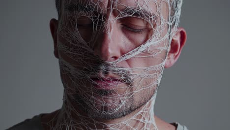 man with closed eyes and web wrapped around head, conveying themes of confinement, vulnerability, and silent struggle against an unseen force