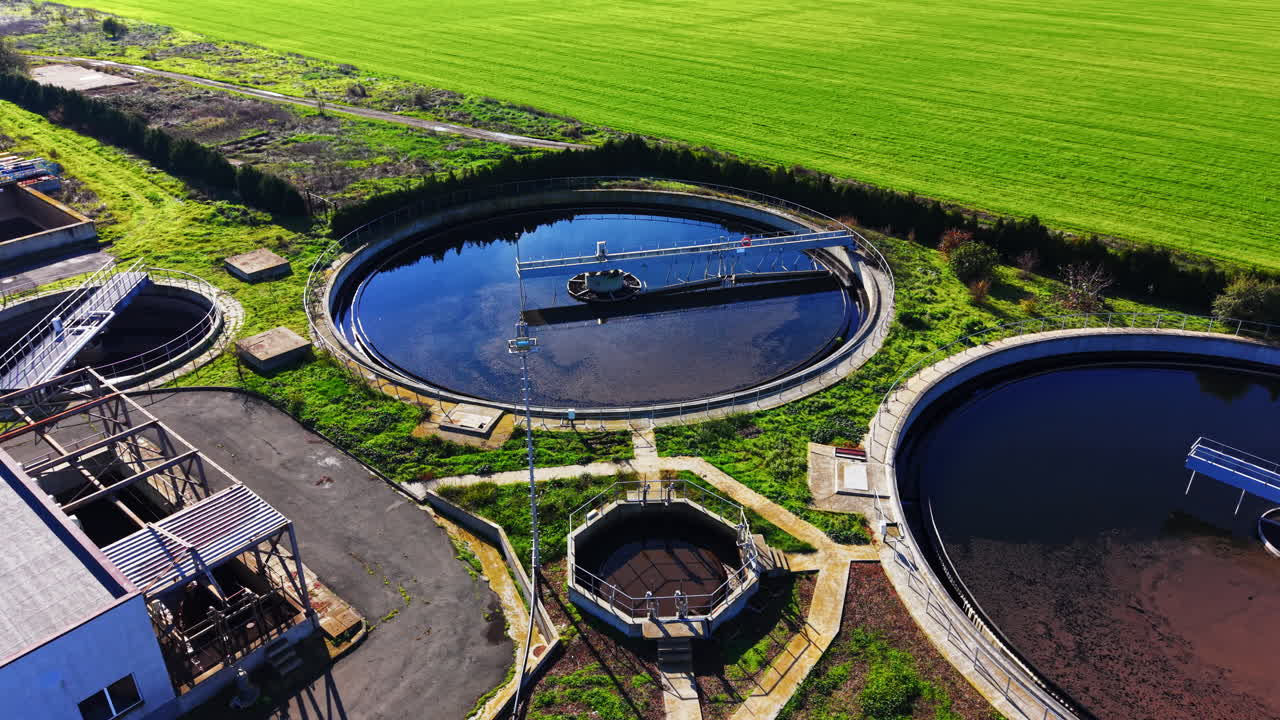 Wide aerial shot showing administrative buildings, circular sedimentation tanks, and rectangular basins under a clear blue sky