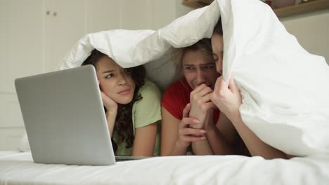 Three-best-friend-woman-on-bed-watching-horror-movie-on-laptop-with-shocked-expression-on-face