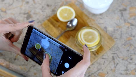 close-up of woman hand with phone making photo slices of lemon in jar.