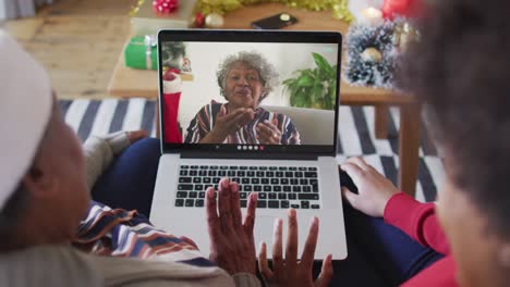 madre y hija afroamericanas usando una computadora portátil para una videollamada de navidad con una mujer en la pantalla