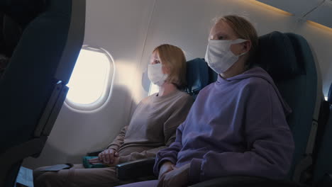 tired mother and daughter fly on a plane. they are wearing protective masks. traveling during the coronavirus pandemic