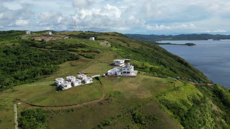 Aerial-orbit-of-uniform-white-glamping-homes-on-secluded-ocean-view-mountain-peak