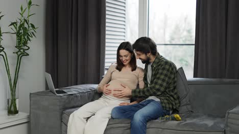 Pregnant-woman-with-large-belly-and-husband-sitting-on-sofa-waiting-for-movements