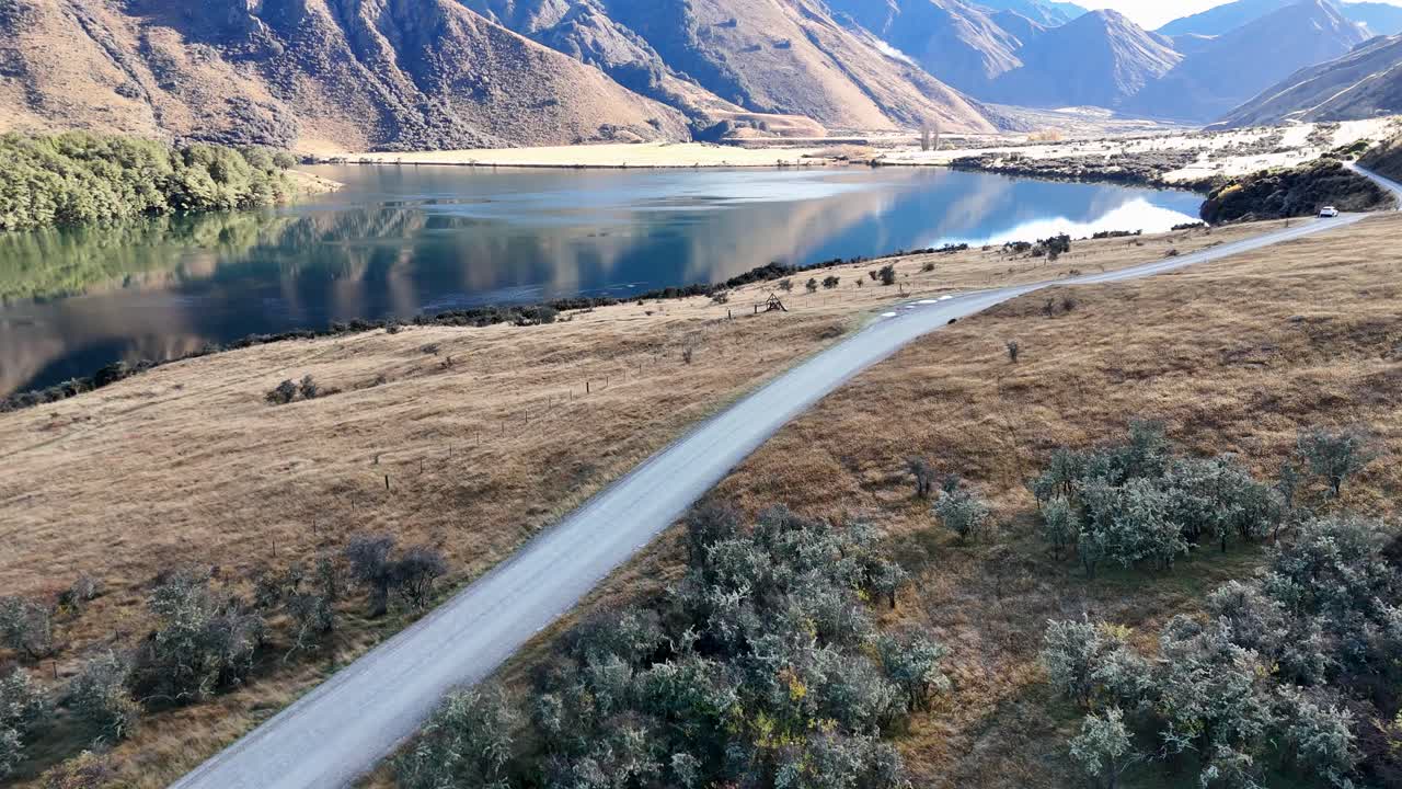 Aerial view of a winding road beside Lake Moke, surrounded by mountains under clear skies, showcasing serene natural beauty