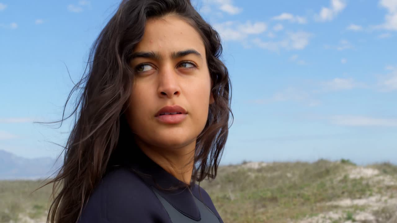 surfista femenina con tabla de surf de pie en la playa 4k