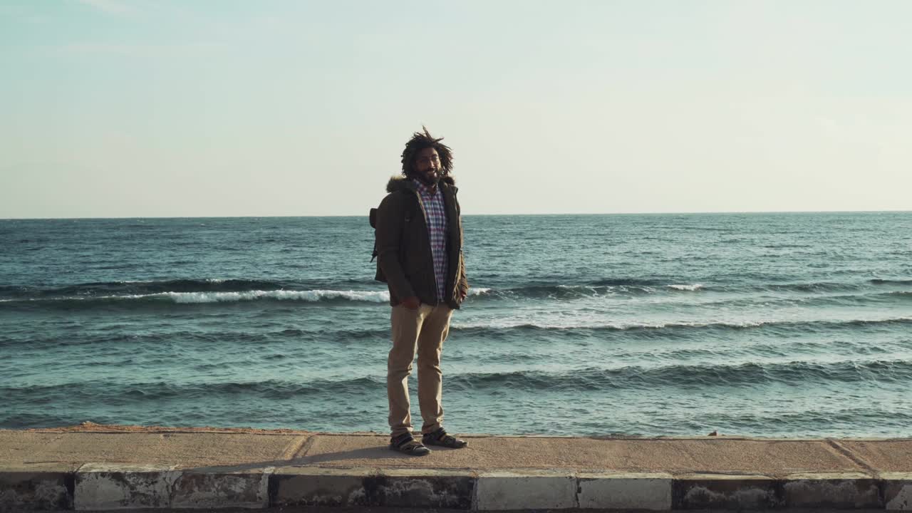 흑인 중동 남성의 초상화가 뒤에 바다가 있는 도로에 서 있습니다.