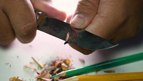 footage of hands slowly sharpening a pencil and some coloured pencils with a sharp knife