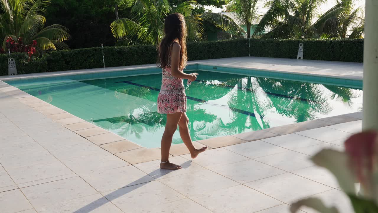 Junge Frau im Urlaub, die an einem Außenpool in einem tropischen Reiseziel entlanggeht