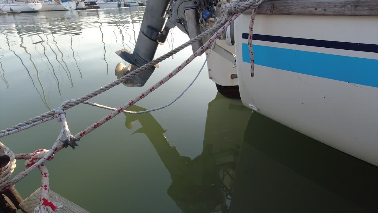 la parte trasera de un yate con un motor fuera de borda atado con cuerdas a un amarre ligeramente balanceado a medida que el agua se mueve por debajo