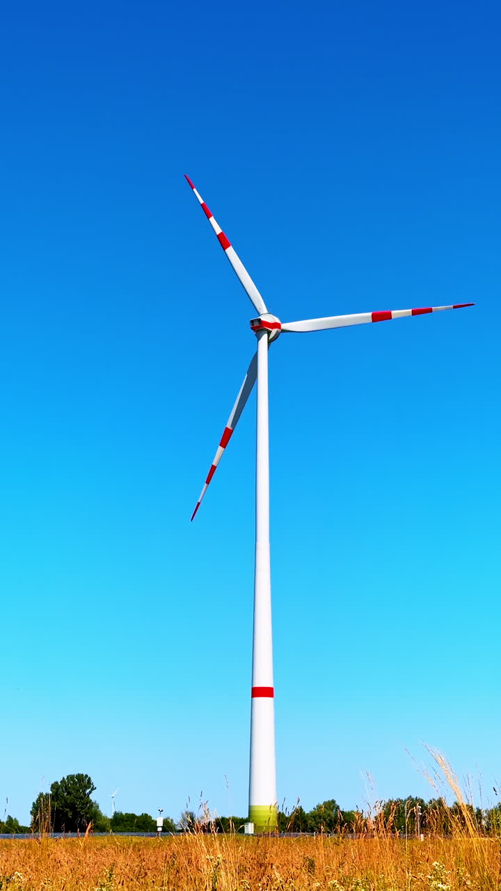 Single wind turbine rotating in the field. Low angle view at one wind mill producing renewable energy. Vertical video