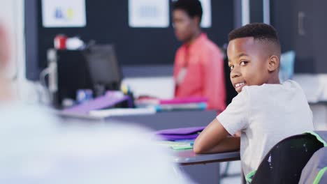 portrait of diverse female teacher and happy schoolchildren at desks in school classroom