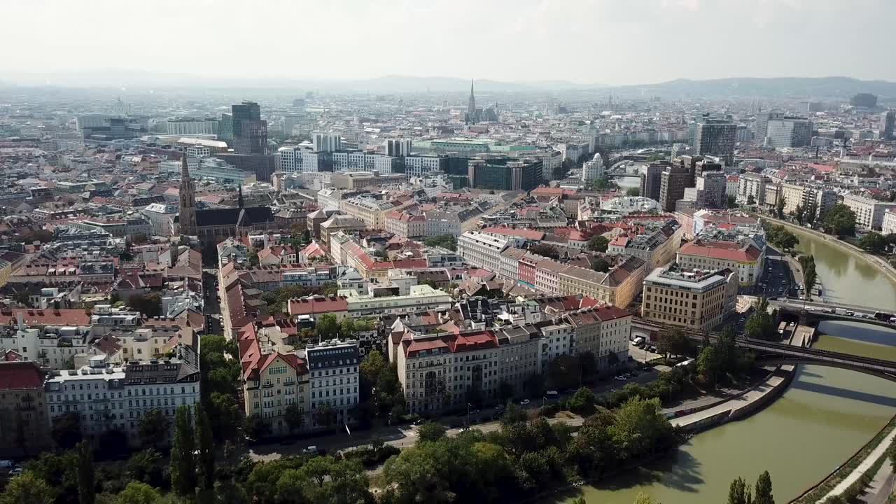 Aerial flyover shot of Vienna City with colorful houses and apartment buildings beside river. Historic church and downtown in background. Wide shot. Austria,Europe.