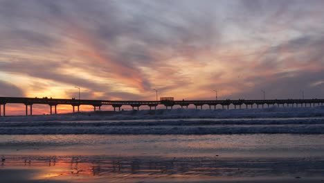 surfers surfing by pier. ocean water waves, people and sky at sunset. california