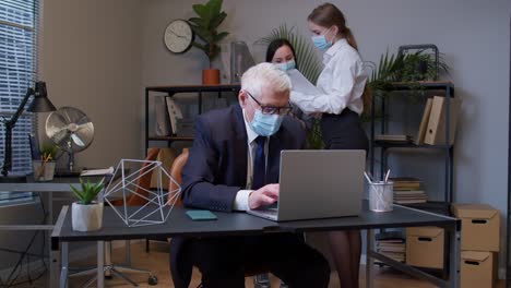 Jefe-Anciano-Con-Máscara-Médica-Trabajando-En-Una-Computadora-Portátil-En-La-Oficina-Durante-La-Pandemia-Del-Coronavirus