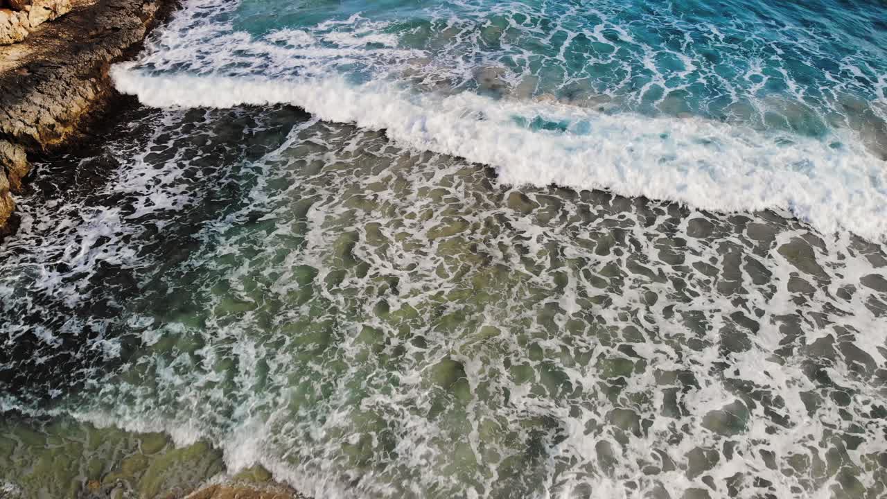 aerial drone shot of a rocky coastline in Majorca with waves crashing onto the rocks and sandy beach of the Mediterranean