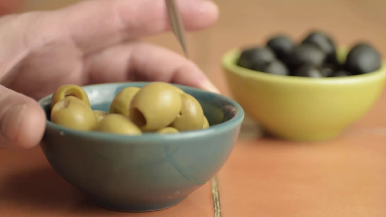 Hand snacking on olives with fork close up shot