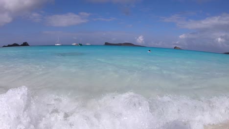a tourist is snorkeling on a turquoise and clear water beach of the galapagos islands. transparent waves are crashing into the shore. some islands and cruises are seen on the back.