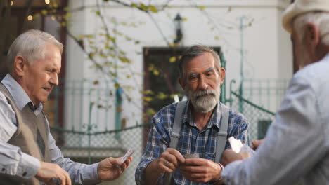 Abuelos-Jubilados-Jugando-A-Las-Cartas-Y-Pensando-Mucho-Mientras-Se-Sientan-Afuera-En-El-Bonito-Patio