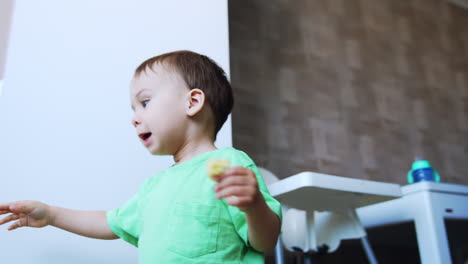 pretty toddler boy sits on the kitchen floor. kid pushes his high chair then stands up to the fridge. low angle view.