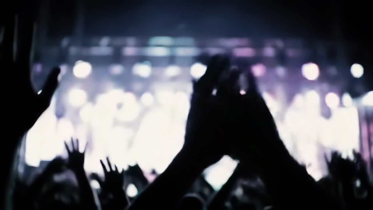 Silhouetted hands clapping and rising during live music concert, capturing collective energy and shared excitement of audience enjoying performance