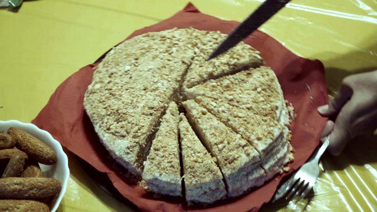 la mujer corta un cuchillo grande en partes iguales de pastel, que vale en el plato con rojo con una servilleta en manteles amarillos. 4k. 25 fps.