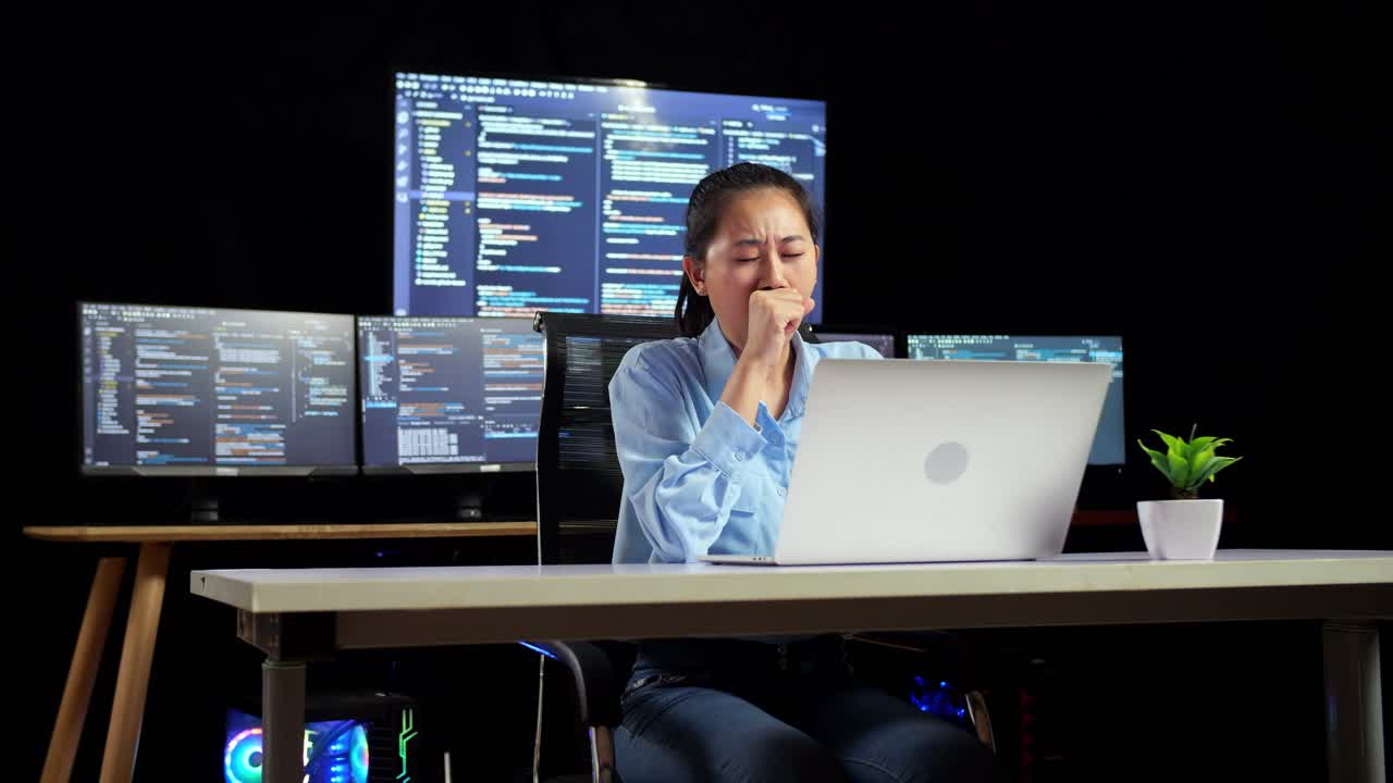 Asian Female Programmer Yawning And Sleeping While Writing Code By A Laptop Using Multiple Monitors Showing Database On Terminal Window Desktops In The Office
