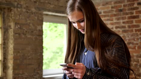 joven hermosa está viendo su teléfono inteligente, concepto de comunicación, fondo de ladrillo