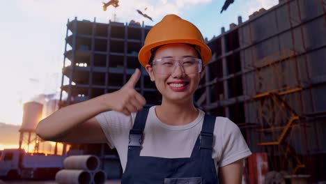 Close Up Of Asian Woman Worker Wearing Goggles And Safety Helmet Smiling And Showing Thumbs Up Gesture While Standing At Construction Site