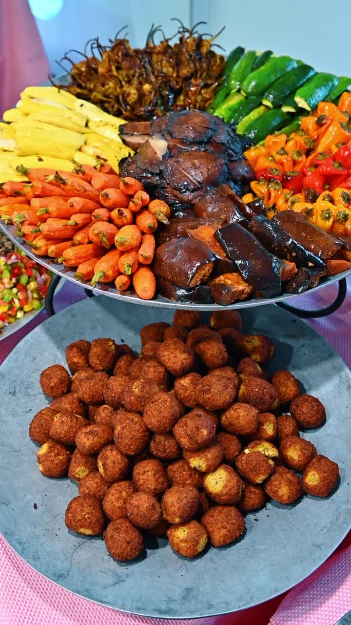 Fuente de verduras asadas variadas con zanahorias, pimientos y falafel frito, servida en bandejas metálicas para buffet.
