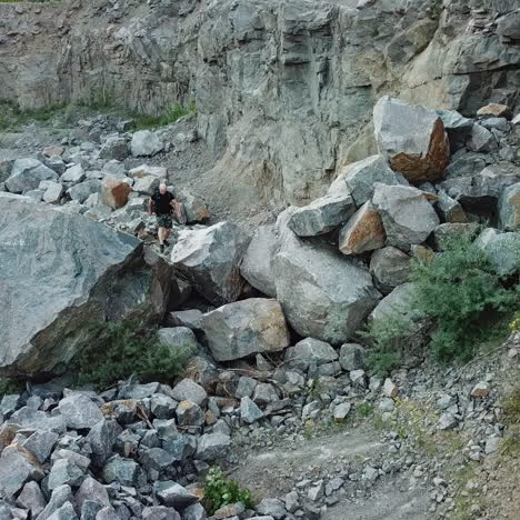 happy male tourist climbing on the rocky mountains. active hiker in casual clothes walking through the stones coming into the biggest one and raises his hands up.