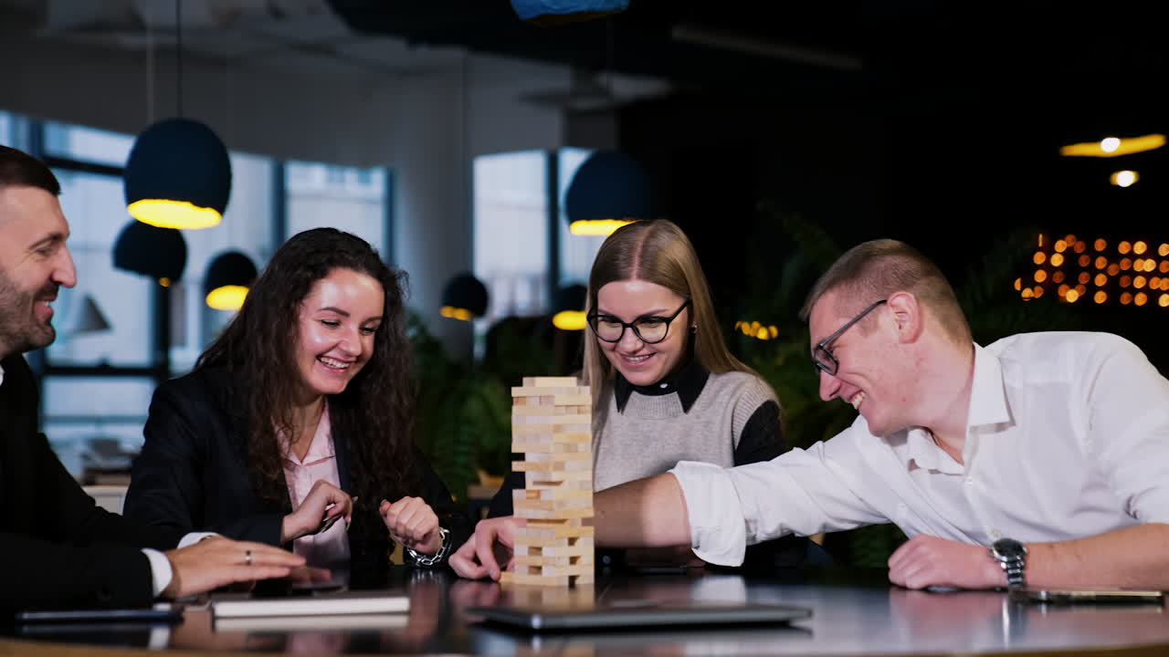 Friendly cheerful company playing game for pleasure. Leisure time spending playing jenga. People take turns to pull the wooden brick.