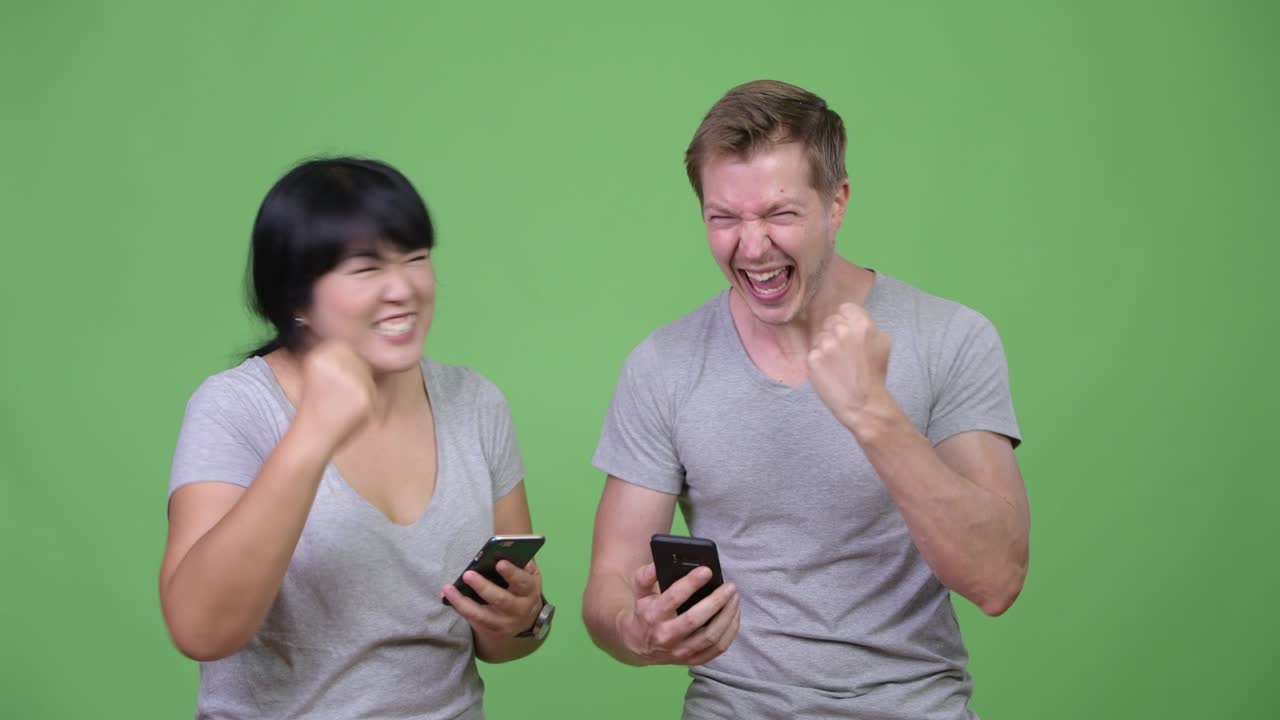 Young multi-ethnic couple using phone and getting good news together