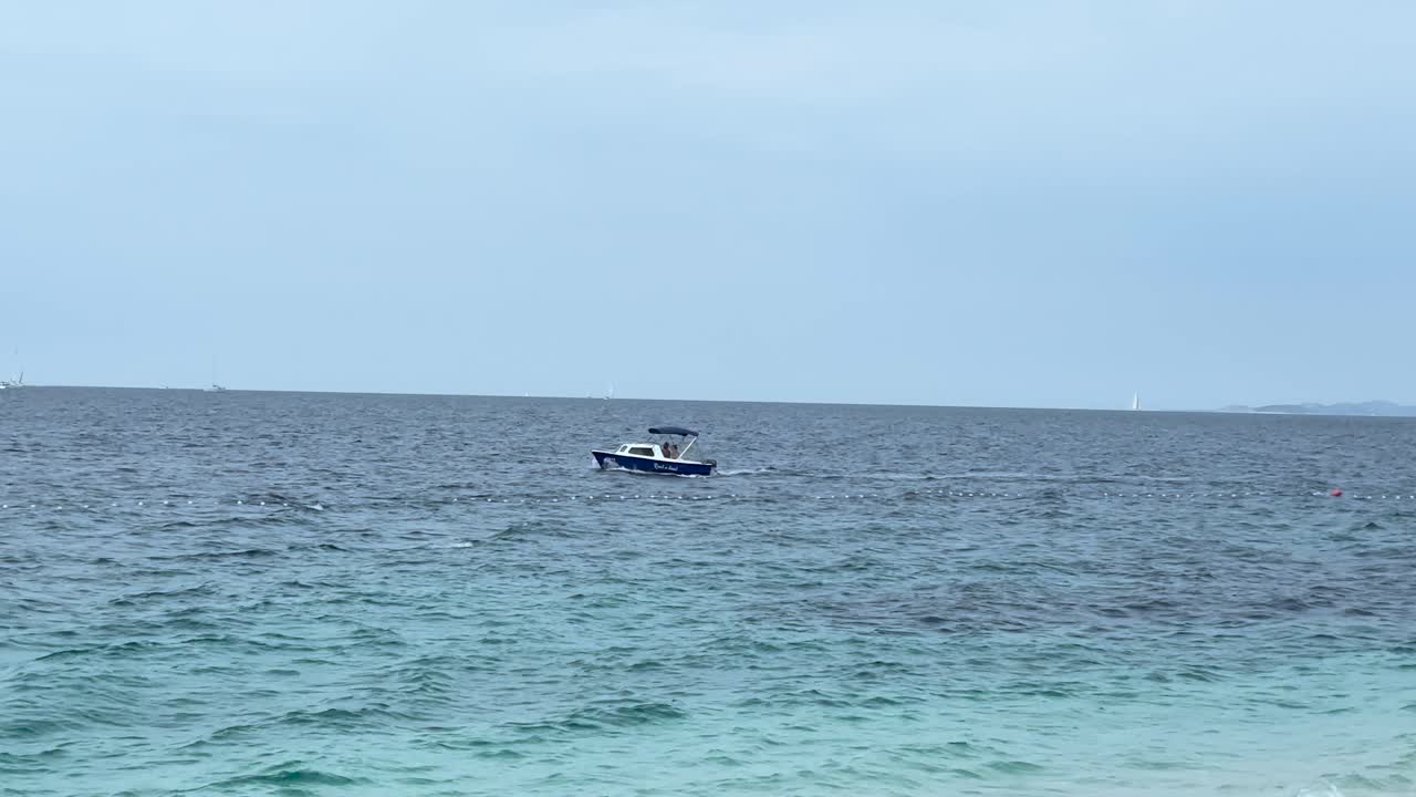 A small motorboat drifts on the open sea with a soft ripple on the water. Overcast sky creates a peaceful maritime atmosphere with distant horizon