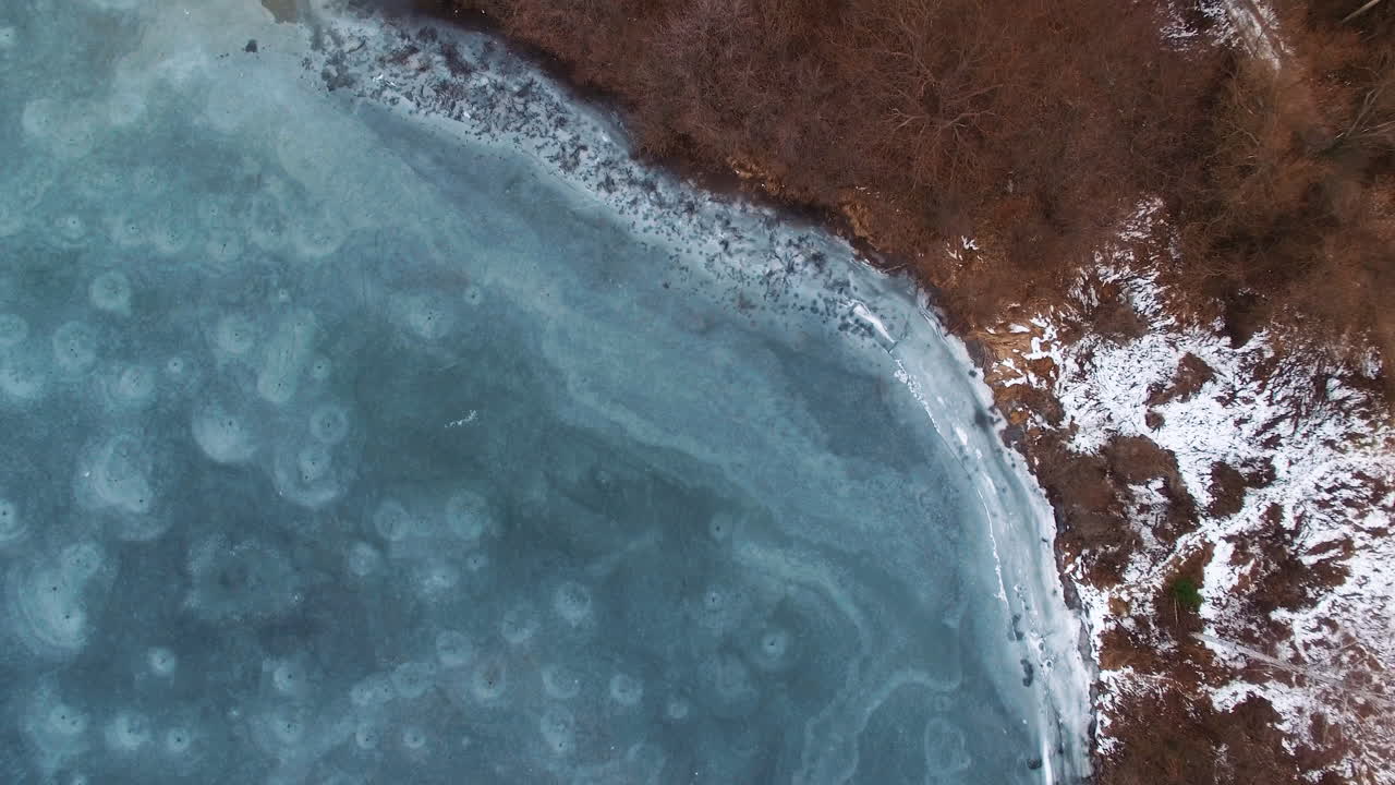 AERIAL: Drone rises above the frozen crystal ice of the lake. Top view. Natural background and patterns