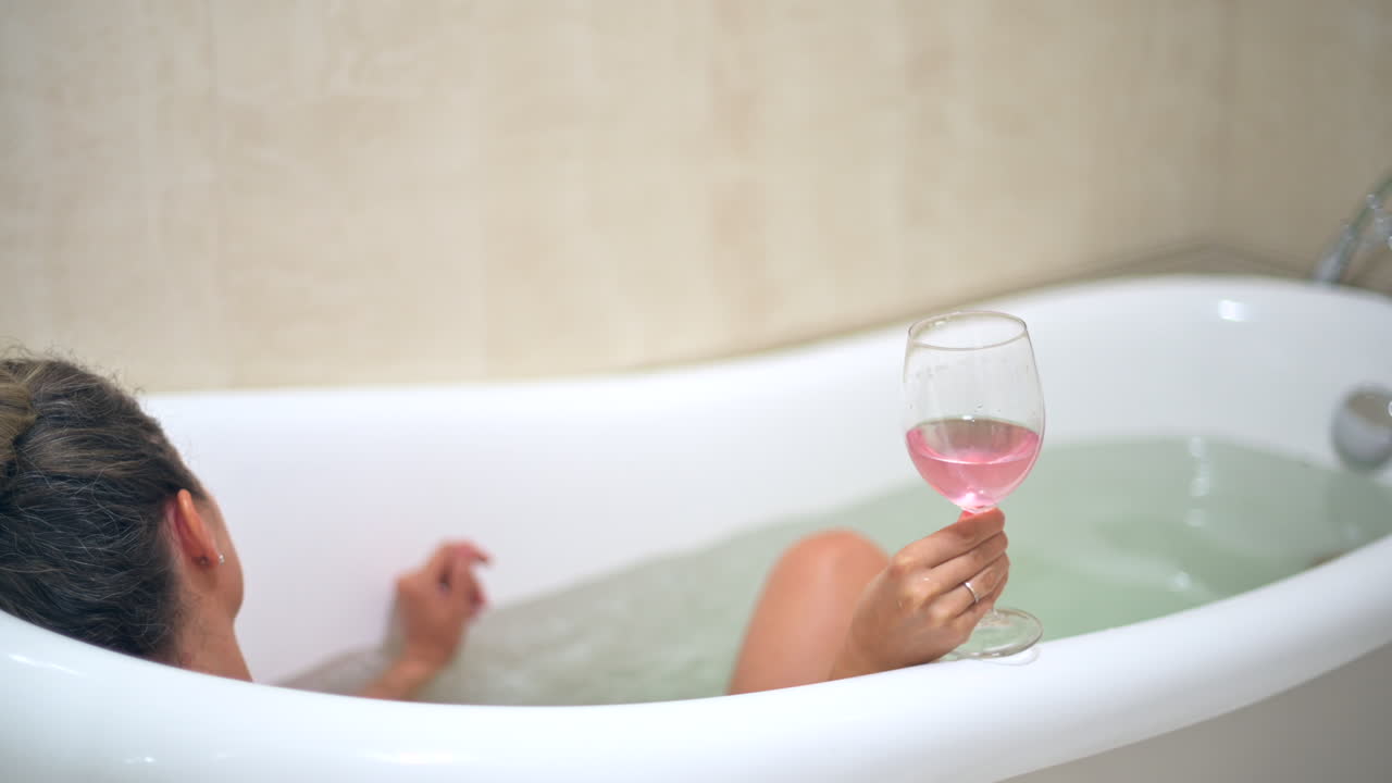 Woman relaxing in the bathtub, drinking rose wine