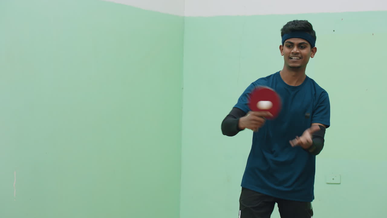 Focused tennis player in blue sportswear swings paddle to strike ball during intense indoor match, displaying concentration, agility, and determination in competitive training atmosphere