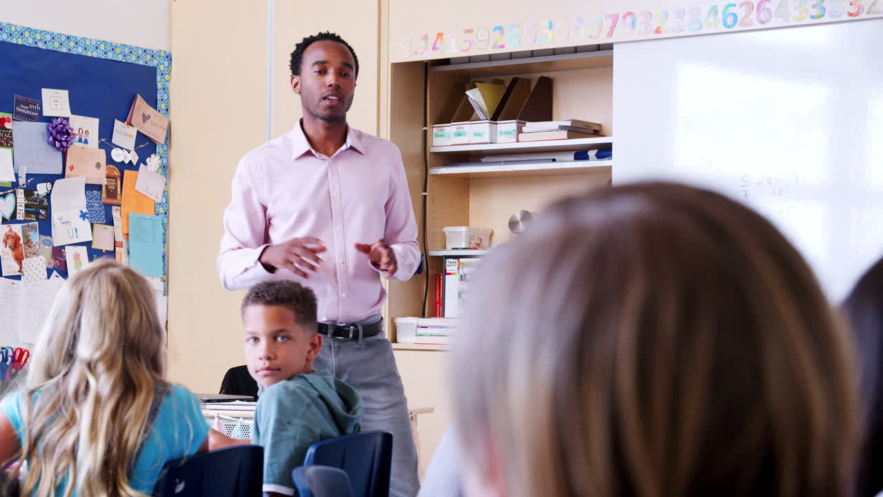 Male teacher points to boy with hand raised in school class