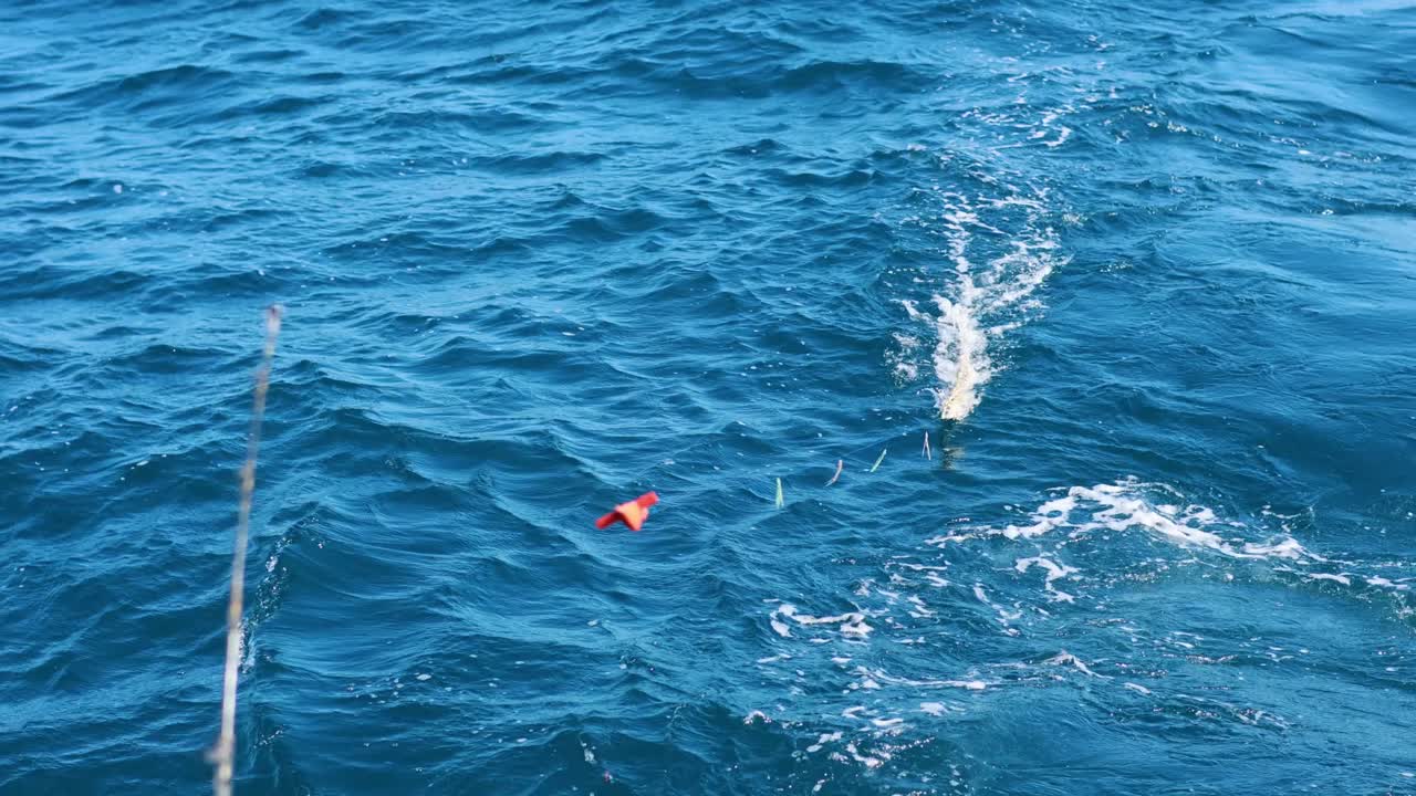 A fishing line dances across the vibrant blue ocean, capturing dynamic movements and splashes under bright daylight in Phuket