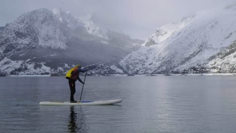 man on paddle board between water and mountains on coast