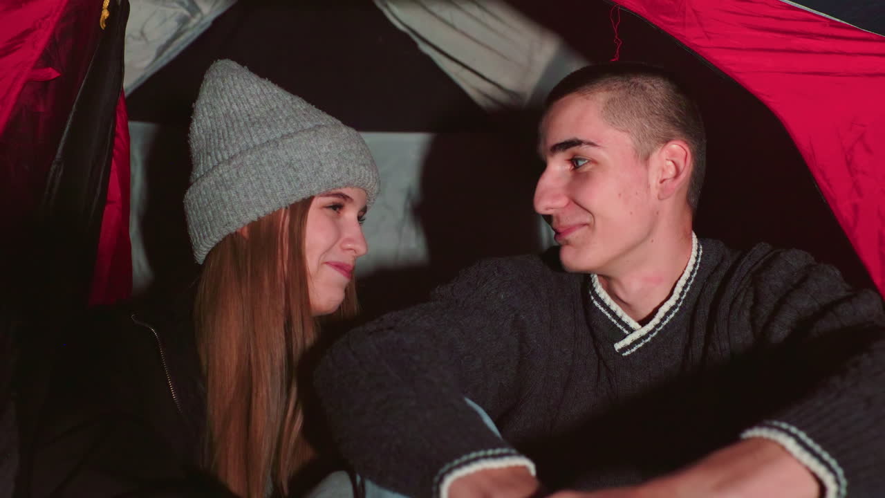Young couple enjoying warm intimate moment inside tent at night as they look at each other with soft smiles and silent affection, capturing peaceful emotional connection