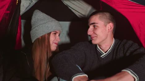 young couple enjoying warm intimate moment inside tent at night as they look at each other with soft smiles and silent affection, capturing peaceful emotional connection