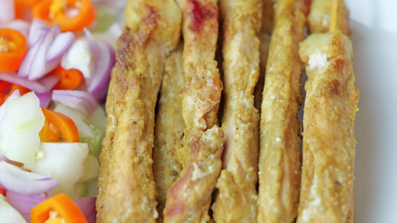 Close-up of many grilled pork satay skewers arranged together, featuring golden charred edges, tender meat, and a rich peanut dipping sauce.