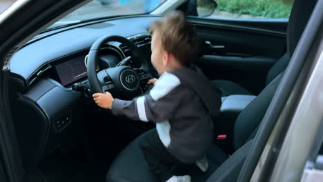 happy caucasian toddler sitting at the steering wheel of a car. baby boy jumps excitedly moving the wheel and smiling to camera.