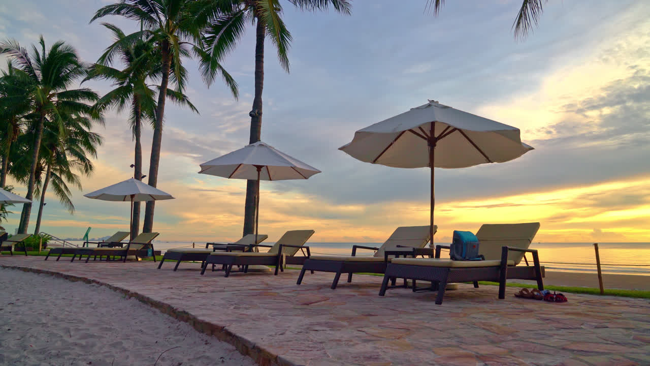 일몰 또는 일출 시간에 바다 해변 근처에서 레저 여행 및 휴가를 보내기 위해 리조트 호텔의 수영장 주변에 있는 우산과 의자