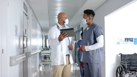 Diverse-doctors-discussing-work-and-using-tablet-in-corridor-at-hospital,-slow-motion