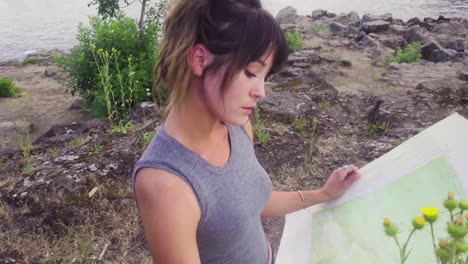 cute hipster girl looking at a paper map of the park she is exploring