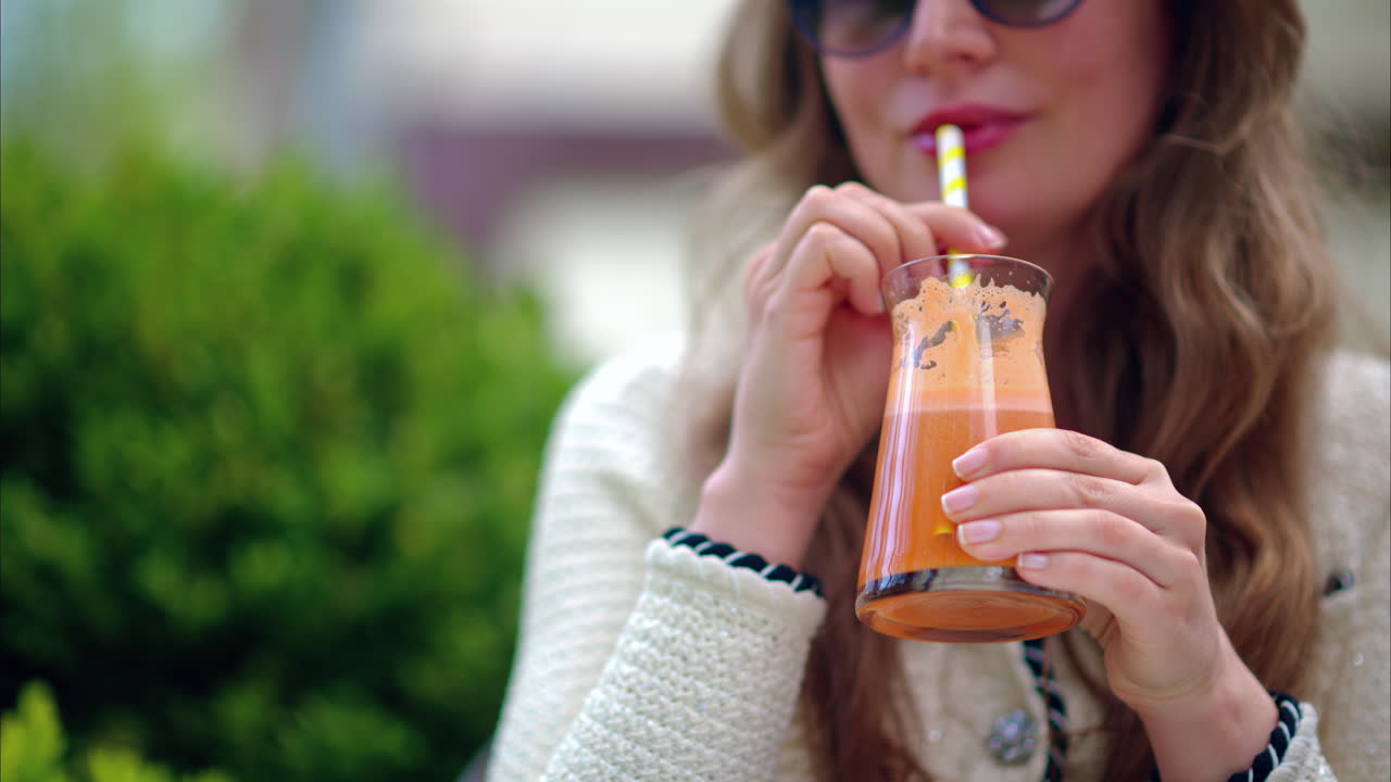 Woman drinking an orange juice using of a straw, at a cafe, outside